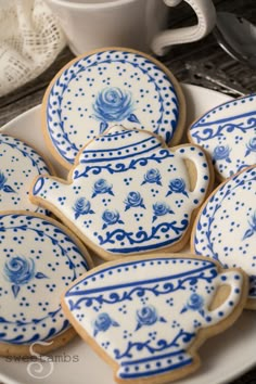 cookies decorated with blue and white designs are on a plate next to silver utensils