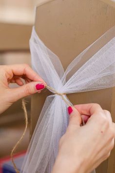 a woman is tying a piece of white tulle to a box with twine