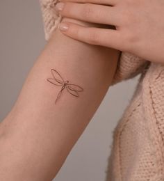 a woman's arm with a small dragonfly tattoo on the left side of her arm