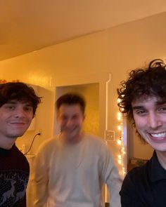 three men are standing in a room with lights on the wall and one is smiling at the camera