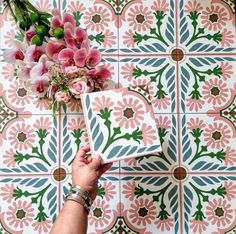 a hand holding a bouquet of flowers on top of a tiled wall with pink and green designs