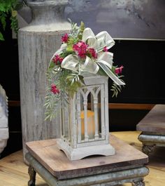 a white lantern with flowers in it sitting on top of a wooden table next to a vase