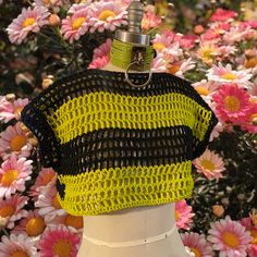 a yellow and black crochet top on a mannequin with flowers in the background