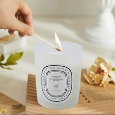 a person lighting a candle with a match stick in front of it on a wooden tray