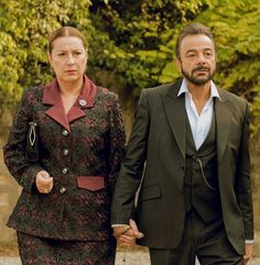 a man and woman holding hands while walking down the street with trees in the background