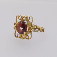 Indulge in the timeless beauty of the Art Nouveau era with this exquisite vintage ring. Meticulously crafted from hallmarked 9ct yellow gold, this ring features a lustrous Cabochon garnet gemstone that exudes vintage charm, making it a perfect addition to any outfit. Key Features: - Metal: Hallmarked 9ct Yellow Gold - Gemstone: Cabochon Garnet - Garnet Dimensions: Approximately 7.8mm by 6.4mm - Ring Size: UK Size M/N - Weight: 2.8 grams - Head Dimensions: Approximately 15.1mm by 13.2mm This ring Antique Ruby Rings With Polished Finish, Formal Yellow Gold Ruby Ring With Cabochon, Antique Yellow Gold Ruby Ring With Polished Finish, 14k Gold Cabochon Red Ring, 14k Gold Red Cabochon Ring, 14k Gold Rings With Red Cabochon, Formal Red Birthstone Ring With Polished Finish, Formal Red Polished Birthstone Ring, Red Cabochon Ruby Ring In 14k Gold