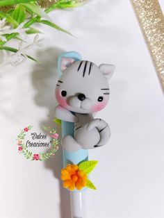 a white cat figurine sitting on top of a pen with flowers in the background