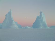 icebergs are floating in the ocean at sunset with a half moon visible above them