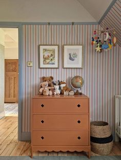 there is a dresser with stuffed animals on it in the room that has striped walls