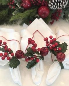 three napkins with holly and berries on them are sitting next to pine cones, evergreen leaves, and red berries