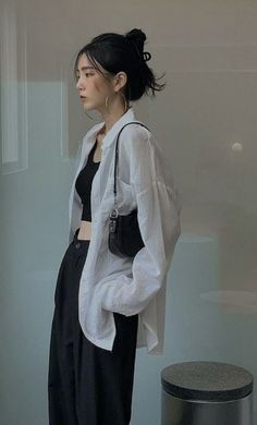 a woman standing in front of a glass wall wearing black pants and a white shirt