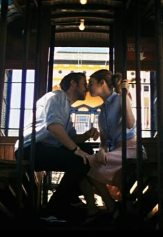 two people are kissing on the stairs in a building with large windows and wood trimmings