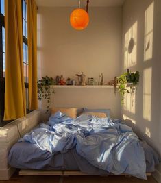 an unmade bed with blue sheets and yellow curtains in a white room next to a window