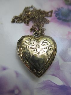 Vintage heart locket necklace in gold fill on silver with a Carl Art makers mark. This pretty heart locket is crafted with a puffed style with engraved flowers accenting a single heart cartouche. Tiny leaves and a detailed border offer the quality of the craftsmanship of a vintage piece. The heart is not monogrammed with initials and can be personalized if you so choose. Inside you will find two spots for photos with frames but no covers. This heart shaped keepsake locket measures seven eighths of an inch by .75'' with the bail. It suspends from an app. 16- 5/8'' fine link chain that is stamped for gold fill on the clasp. The locket exhibits slight wear that adds to the charm of this older vintage piece. Just lovely for a first locket and a lovely accessory to accent romantic and feminine Heart Necklace With Picture Inside, Lockets Gold, Vintage Heart Locket, Random Outfits, Flowers Heart, Pretty Heart, Picture Locket, Engraved Flower, Heart Locket Necklace