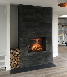 a fire place in a living room with wood stacked on the floor next to it