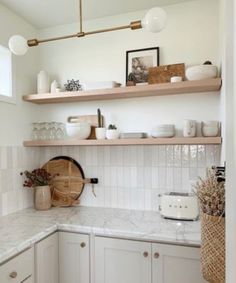 a white kitchen with wooden shelves and marble counter tops