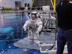 two men in spacesuits standing next to each other on a surface with water