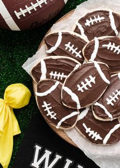 football cookies decorated with chocolate frosting on top of a plate next to a yellow bow