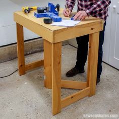 a man sitting at a wooden table writing on a piece of paper with construction tools nearby