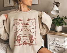 "🔮Ouija Board Sweatshirt | Witchy Pullover🔮 Want the same design on a t-shirt? You can find it here:  https://www.etsy.com/listing/1300222489/ouija-board-tee-halloween-party-t-shirt ✦ This unisex heavy blend crewneck sweatshirt is pure comfort and fits like a well-loved favorite. Super soft cotton and excellent quality print make it the perfect gift for your hubby, friends, and loved ones.  ✦ Want an OVERSIZED sweatshirt? Then you should pick 2 sizes larger than your normal fit size. Also make sure you check the color and size chart for correct size. The collar is ribbed knit, so it retains its shape even after washing. There are no itchy side seams on these sweaters.  :: 50% cotton, 50% polyester :: Medium-heavy fabric (8.0 oz/yd² (271.25 g/m :: Loose fit :: Sewn-in label :: Runs true t Personalized Dog Gift, Mom Sweater, Pumpkin Sweatshirts, Christmas Puppy, Mama Gifts, Fall Sweatshirt, Halloween Sweatshirt, Retro Halloween, Look Vintage