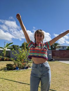 a woman is standing in the grass with her arms up and she has both hands raised