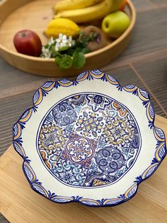 an ornate blue and white plate sitting on top of a wooden table next to a bowl of fruit