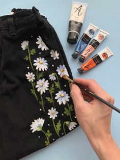 someone is painting daisies on the side of a black jean pants with paint and pencils