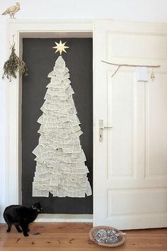 a black cat standing in front of a door with a christmas tree made out of books