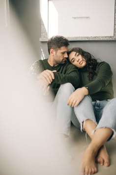 a man and woman sitting next to each other with their arms around each other on the floor