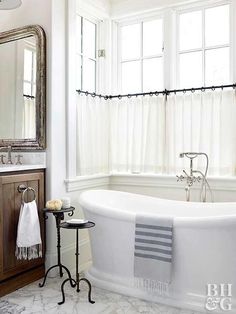 a white bath tub sitting under a bathroom window next to a wooden sink vanity and mirror