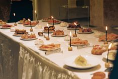 a table topped with lots of plates filled with food and lit candles on top of it