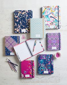 various notebooks and pens are arranged on a white wooden surface, including one with colorful designs