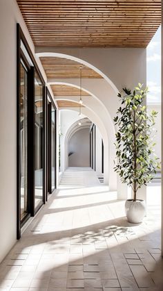 an arched hallway with white walls and tile flooring is flanked by a potted plant