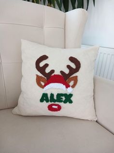 a white couch with a christmas pillow on it and a reindeer's head embroidered onto the back