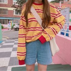 a girl with long brown hair wearing a yellow and red striped sweater, blue denim shorts and white sneakers