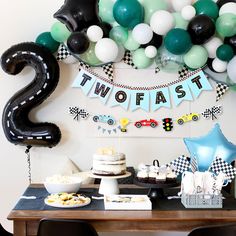 a table topped with balloons and cake next to a sign that says two - fast