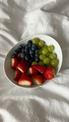 grapes, strawberries and blueberries in a bowl on a white bed sheet top