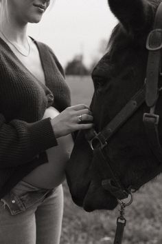 a black and white photo of a woman petting a horse's head in a field