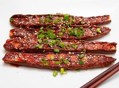 chopsticks on a white plate with meat and green onion garnishes