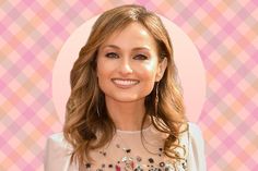 a woman with long brown hair wearing a white dress and smiling at the camera while standing in front of a pink checkered wall