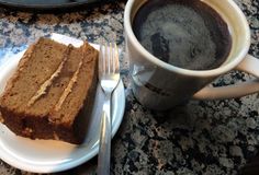 a piece of cake on a plate next to a cup of coffee