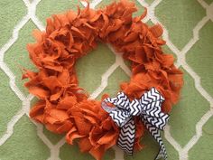 an orange wreath with black and white chevrons is on the floor next to a green wall