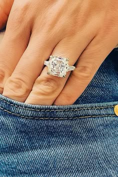 a woman's hand with a diamond ring on her left finger, wearing jeans