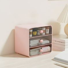 a pink shelf with two drawers on top of it next to a lamp and other items