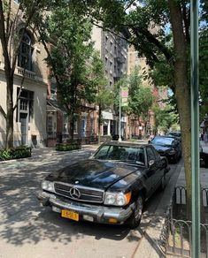 a black car parked on the side of a street next to tall buildings and trees