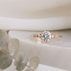 a diamond ring sitting on top of a white table next to eucalyptus leaves and greenery