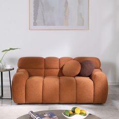 an orange couch sitting in a living room next to a table with fruit on it