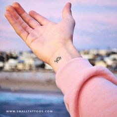 a person's hand with a small tattoo on their left wrist and the ocean in the background