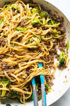 a skillet filled with noodles, meat and broccoli next to tongs