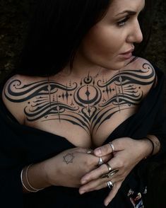 a woman with tattoos on her chest holding her hands in front of her chest and looking at the camera